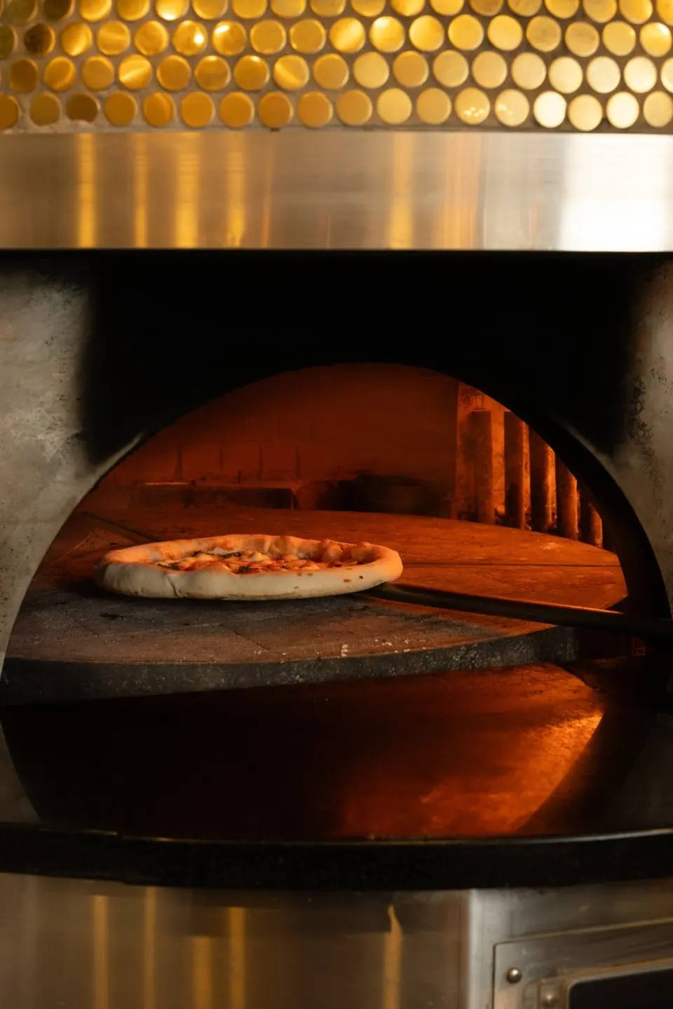 A pizza on the peel at the mouth of the wood-fired oven