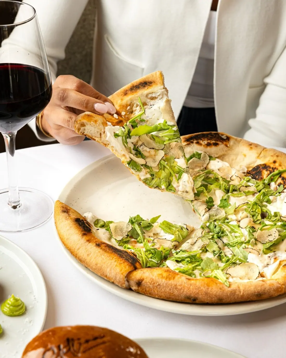 A slice of white pizza with greens being lifted at Stellina